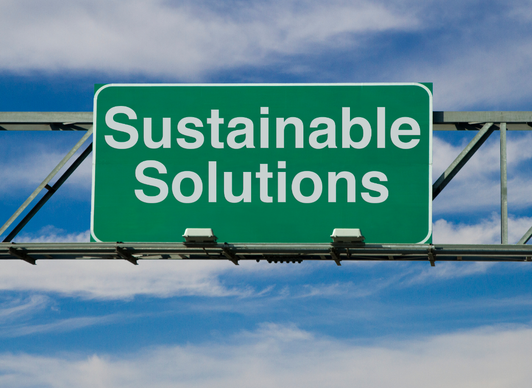 a green highway sign that reads "Sustainable Solutions" in front of a blue and cloudy sky